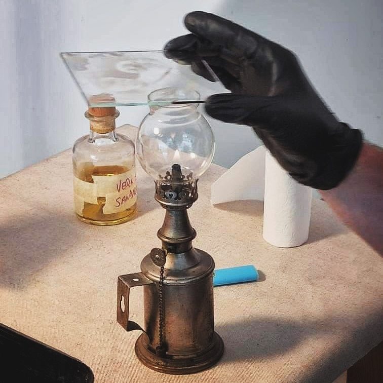 Photo d'une main gantée en noir en train de tenir une plaque de verre au-dessus de la flamme d'une lampe à alcool