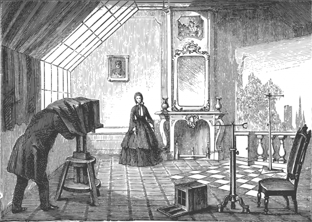 Gravure ancienne : un atelier de photographie, une personne affairée à une chambre photographique et une autre qui prend la pose sous une verrière